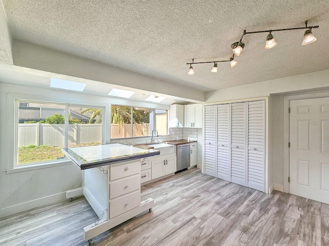 kitchen featuring white cabinetry, stainless steel dishwasher, plenty of natural light, and light wood-type flooring