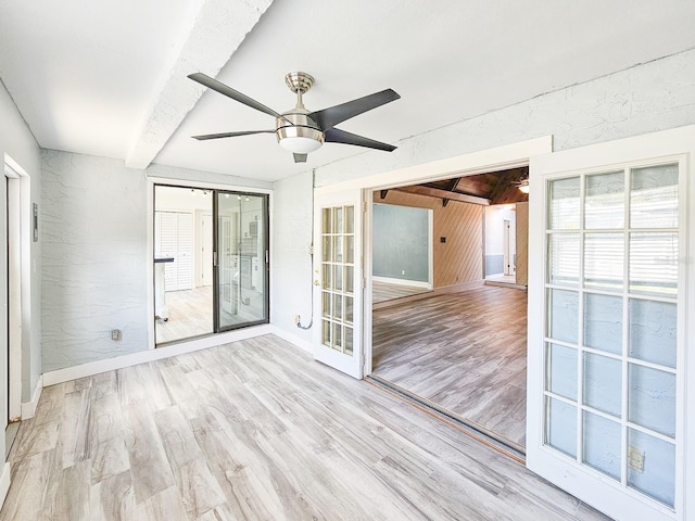 spare room featuring ceiling fan, light hardwood / wood-style floors, beamed ceiling, and wood walls