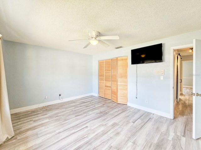 unfurnished bedroom featuring ceiling fan, a closet, a textured ceiling, and light wood-type flooring