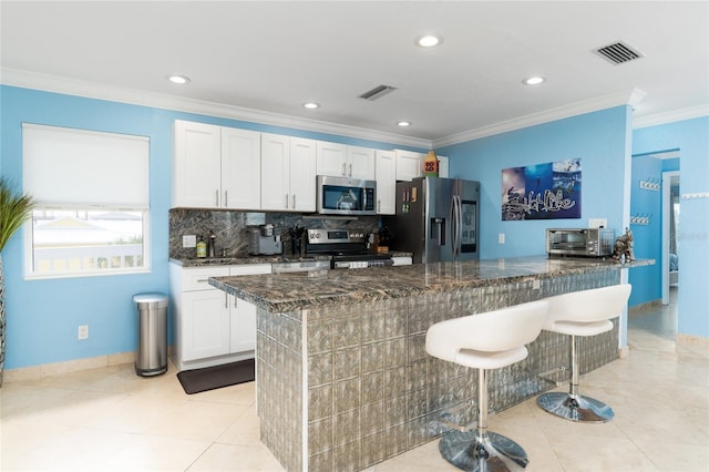 kitchen with stainless steel appliances, a breakfast bar, dark stone counters, and white cabinets