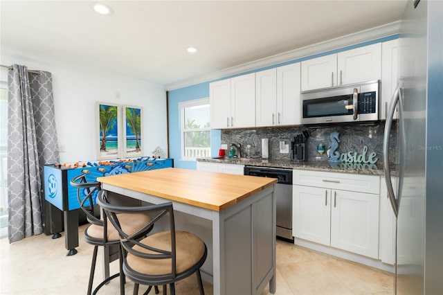 kitchen with wooden counters, white cabinetry, stainless steel appliances, a kitchen breakfast bar, and a center island