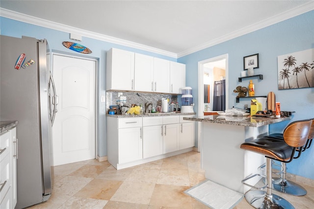 kitchen featuring a breakfast bar, white cabinetry, stone countertops, stainless steel fridge, and kitchen peninsula