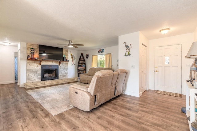 living room with ceiling fan, a stone fireplace, light hardwood / wood-style flooring, and a textured ceiling