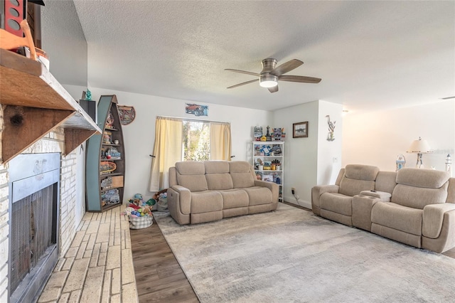 living room featuring a textured ceiling, a fireplace, ceiling fan, and light wood-type flooring