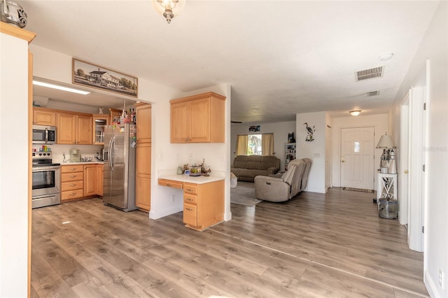 kitchen featuring stainless steel appliances, built in desk, hardwood / wood-style floors, and light brown cabinets