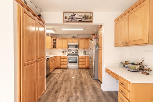 kitchen featuring appliances with stainless steel finishes, light brown cabinetry, built in desk, and light hardwood / wood-style flooring