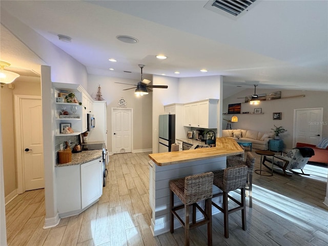 kitchen with a breakfast bar area, vaulted ceiling, kitchen peninsula, stainless steel appliances, and white cabinets