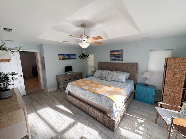 bedroom featuring ceiling fan, a tray ceiling, and light wood-type flooring