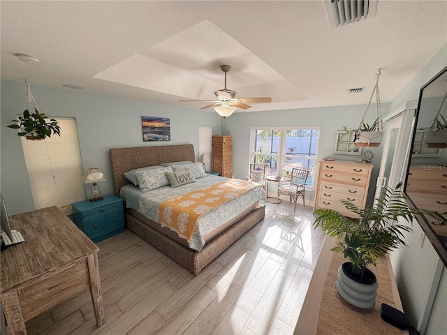 bedroom with light hardwood / wood-style floors, a raised ceiling, and ceiling fan