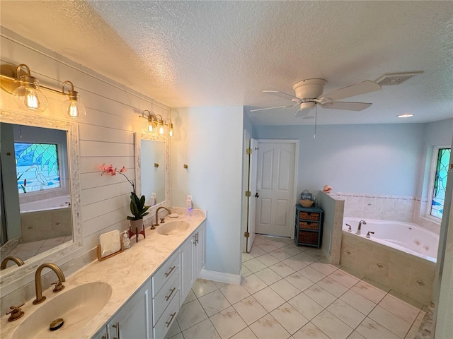 bathroom with tile patterned floors, a textured ceiling, vanity, tiled tub, and ceiling fan