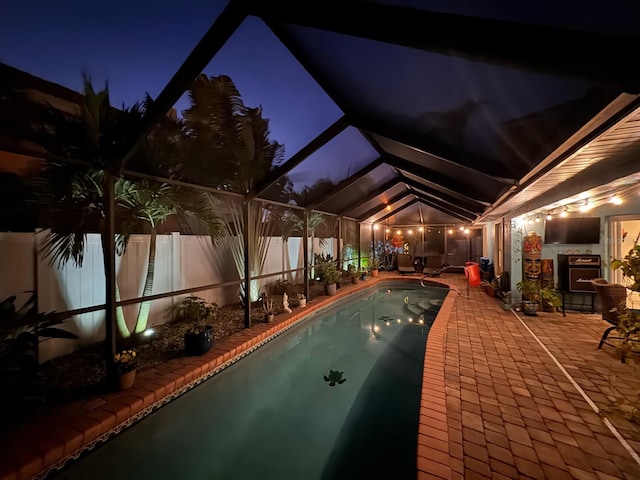 pool at night with glass enclosure and a patio area