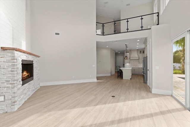 unfurnished living room with light wood-type flooring, a fireplace, baseboards, and a towering ceiling