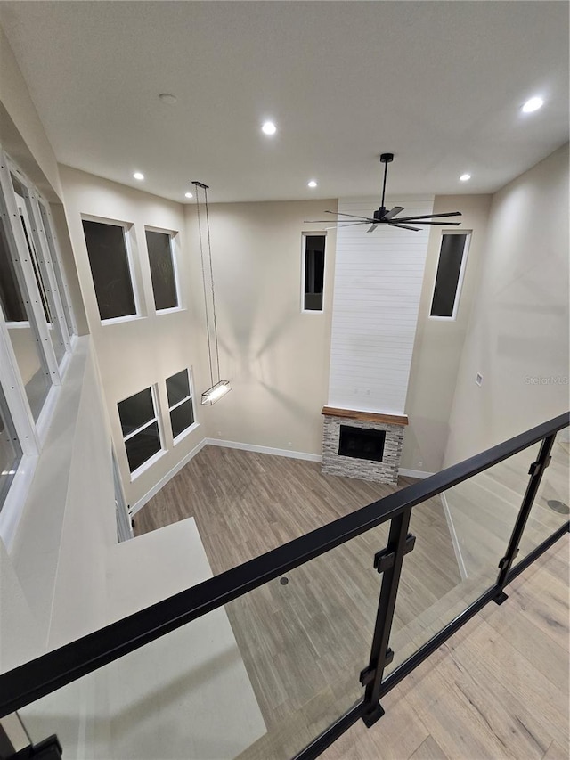 stairs with baseboards, ceiling fan, wood finished floors, a stone fireplace, and recessed lighting