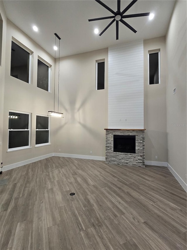 unfurnished living room featuring a stone fireplace, wood finished floors, a high ceiling, and baseboards