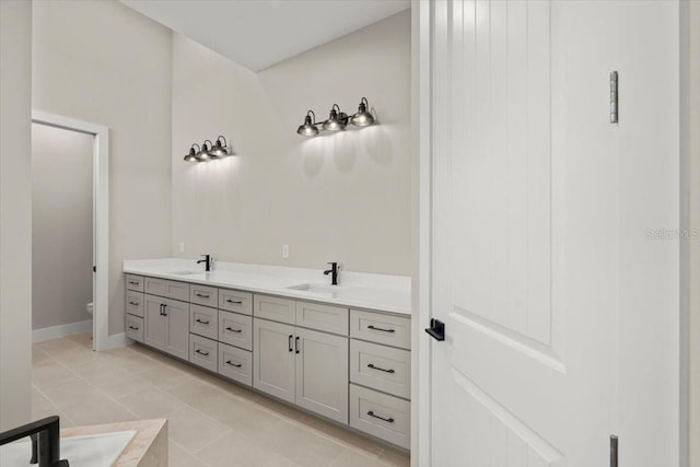 bathroom featuring toilet, double vanity, a sink, and tile patterned floors