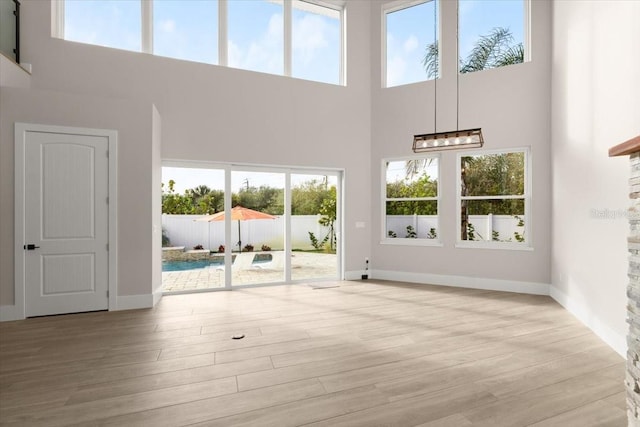 unfurnished living room featuring light wood-style floors, a high ceiling, and baseboards