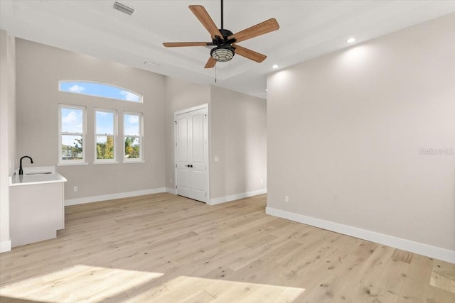 empty room with light wood-style floors, baseboards, visible vents, and a sink