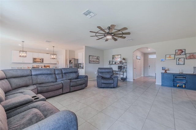 living area with arched walkways, light tile patterned floors, ceiling fan with notable chandelier, visible vents, and baseboards