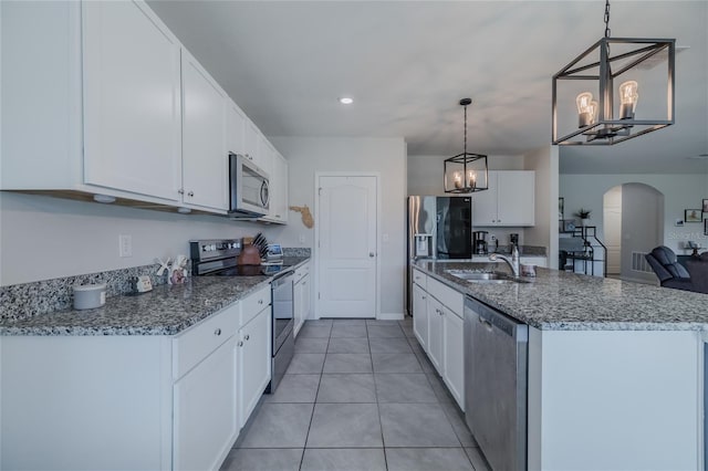 kitchen with arched walkways, a sink, white cabinets, appliances with stainless steel finishes, and decorative light fixtures