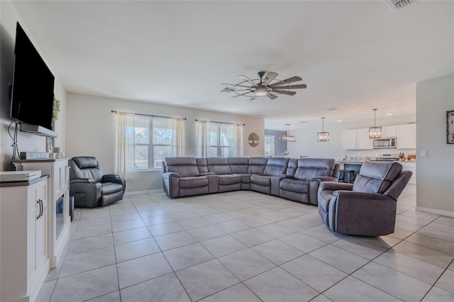 living area featuring light tile patterned floors, ceiling fan with notable chandelier, visible vents, and baseboards