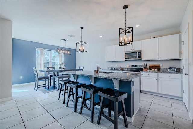 kitchen featuring a center island with sink, white cabinets, dark stone countertops, stainless steel appliances, and pendant lighting