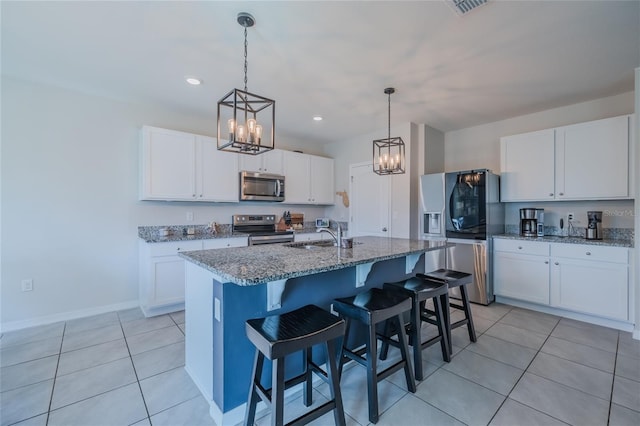 kitchen with light tile patterned floors, stainless steel appliances, white cabinets, light stone countertops, and a center island with sink