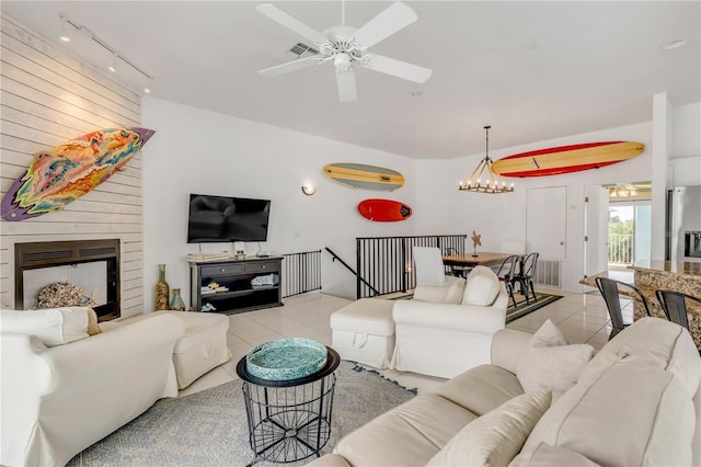 tiled living room featuring a large fireplace, rail lighting, and ceiling fan with notable chandelier