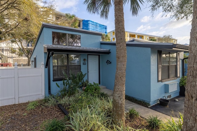 view of front of house with fence, metal roof, and stucco siding