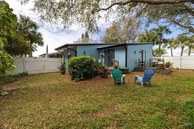 back of house featuring fence private yard, a lawn, and stucco siding