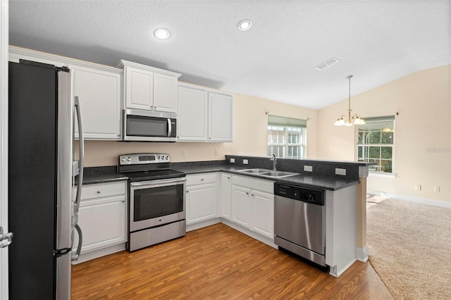 kitchen with sink, white cabinetry, vaulted ceiling, kitchen peninsula, and stainless steel appliances