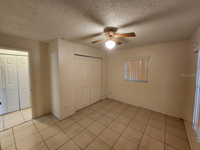 unfurnished bedroom featuring light tile patterned flooring, a textured ceiling, ceiling fan, and a closet