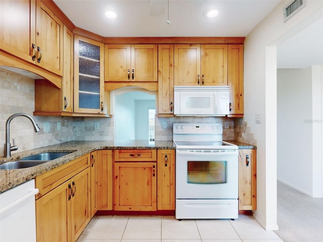 kitchen with white appliances, visible vents, glass insert cabinets, light stone counters, and a sink