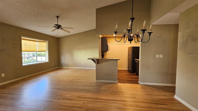 unfurnished living room with lofted ceiling, ceiling fan with notable chandelier, a textured ceiling, and light wood-type flooring