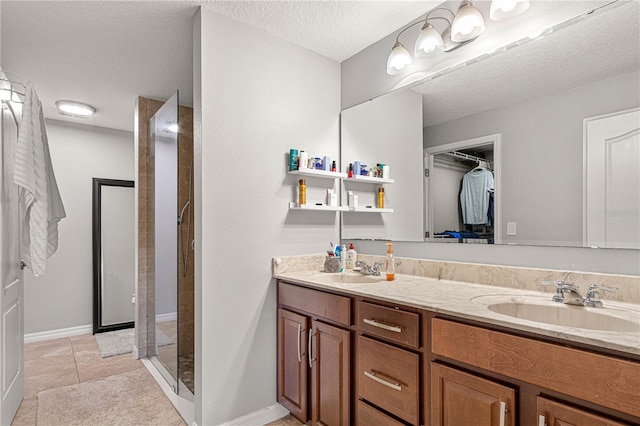 bathroom with double vanity, a tile shower, a sink, a textured ceiling, and tile patterned floors