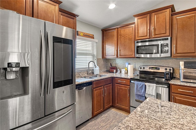 kitchen with brown cabinets, backsplash, appliances with stainless steel finishes, vaulted ceiling, and a sink