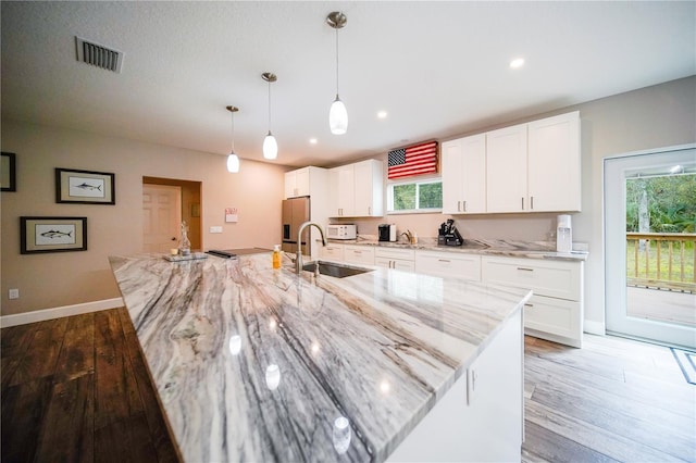 kitchen with light stone countertops, hanging light fixtures, a large island with sink, and white cabinets