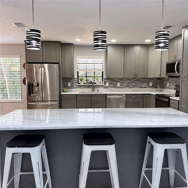 kitchen featuring pendant lighting, sink, a breakfast bar area, light stone counters, and stainless steel appliances