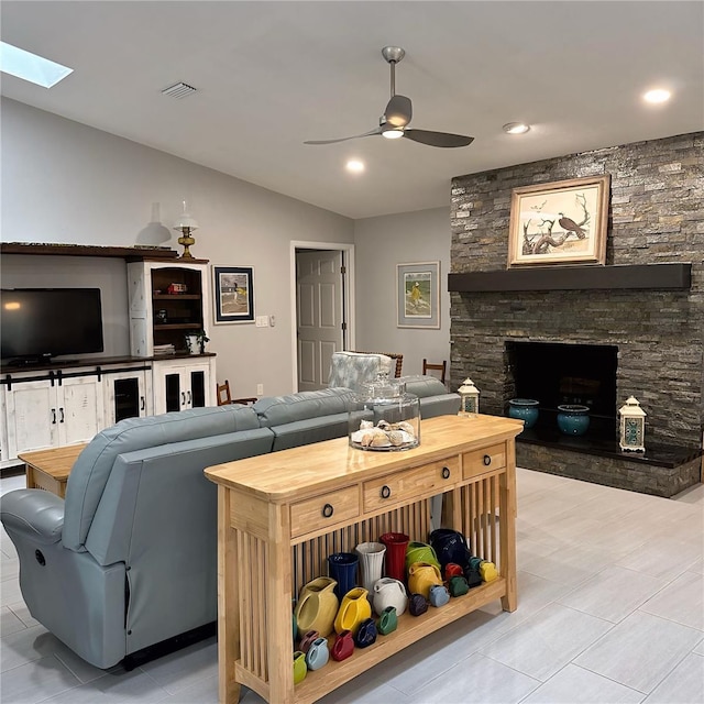 living room with ceiling fan, a fireplace, and vaulted ceiling with skylight