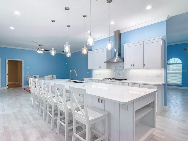 kitchen with sink, white cabinetry, decorative light fixtures, a kitchen island with sink, and wall chimney range hood