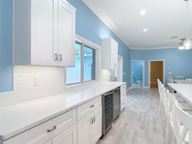 kitchen with white cabinetry, beverage cooler, decorative backsplash, hanging light fixtures, and crown molding