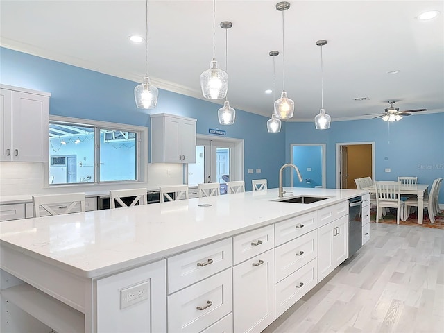 kitchen featuring sink, hanging light fixtures, light stone countertops, an island with sink, and white cabinets