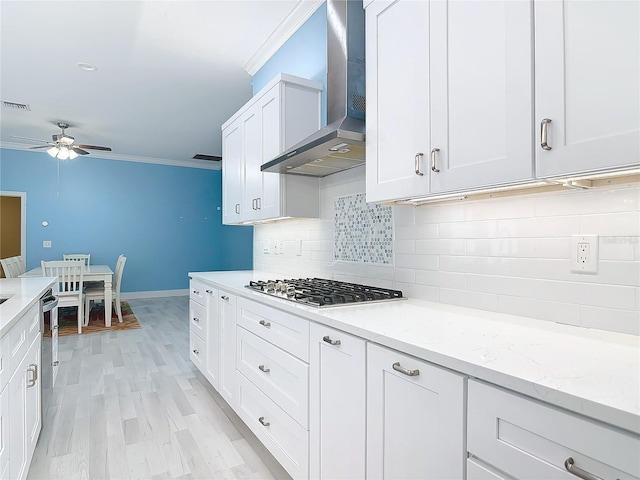 kitchen with stainless steel gas stovetop, white cabinetry, ornamental molding, light stone counters, and wall chimney exhaust hood