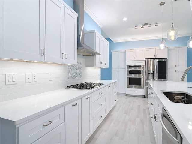 kitchen featuring sink, appliances with stainless steel finishes, pendant lighting, wall chimney range hood, and white cabinets