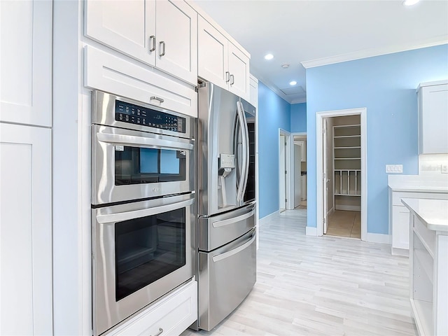 kitchen featuring white cabinetry, appliances with stainless steel finishes, ornamental molding, and light wood-type flooring