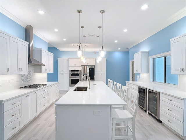 kitchen featuring wine cooler, wall chimney exhaust hood, sink, white cabinetry, and stainless steel appliances