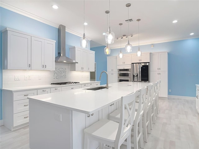 kitchen featuring appliances with stainless steel finishes, sink, hanging light fixtures, a large island, and wall chimney range hood
