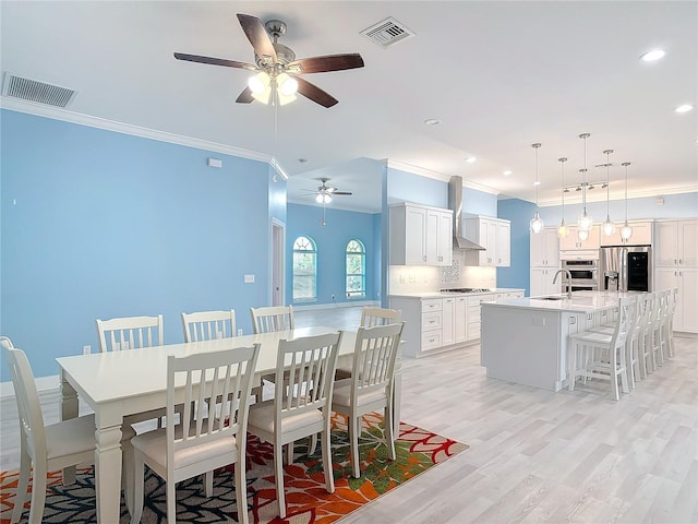 dining space with ceiling fan, ornamental molding, light hardwood / wood-style floors, and sink