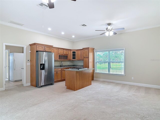 kitchen with a kitchen island, ornamental molding, ceiling fan, stainless steel appliances, and light carpet