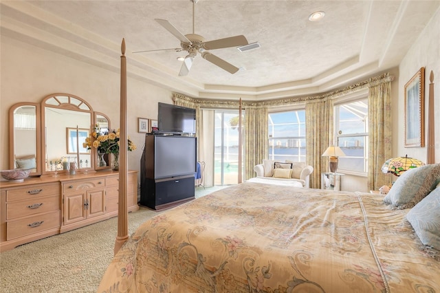 bedroom featuring ceiling fan, a tray ceiling, visible vents, and light colored carpet