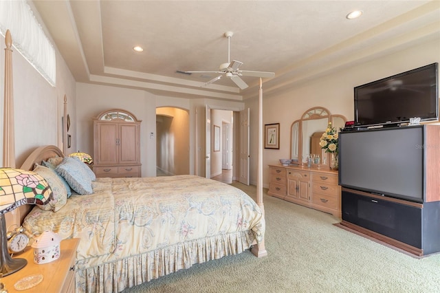 bedroom with recessed lighting, arched walkways, a raised ceiling, and light colored carpet